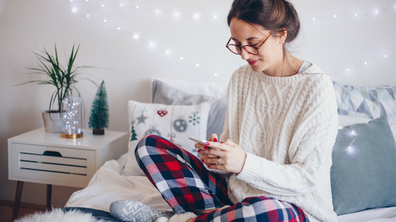 Woman sitting on bed using cell phone for holiday shopping